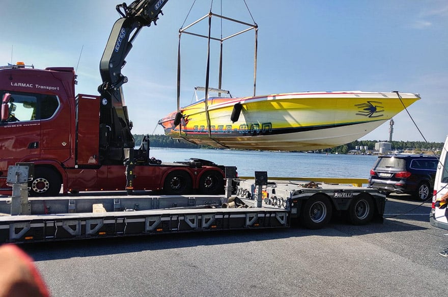 En röd kranbil lyfter en gul båt inför båttransport.