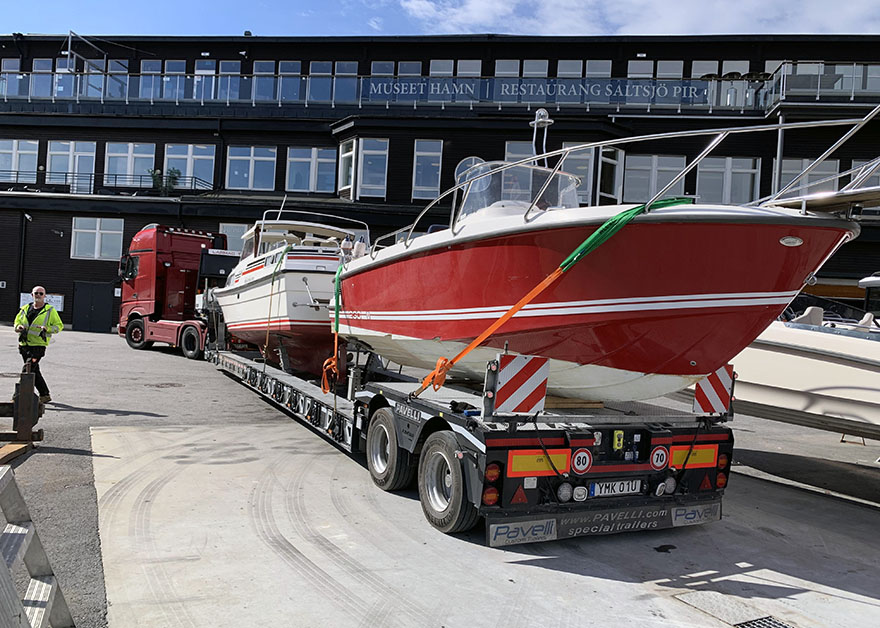 En röd lastbil kör en dubbel båttransport, med två båtar på lasten.